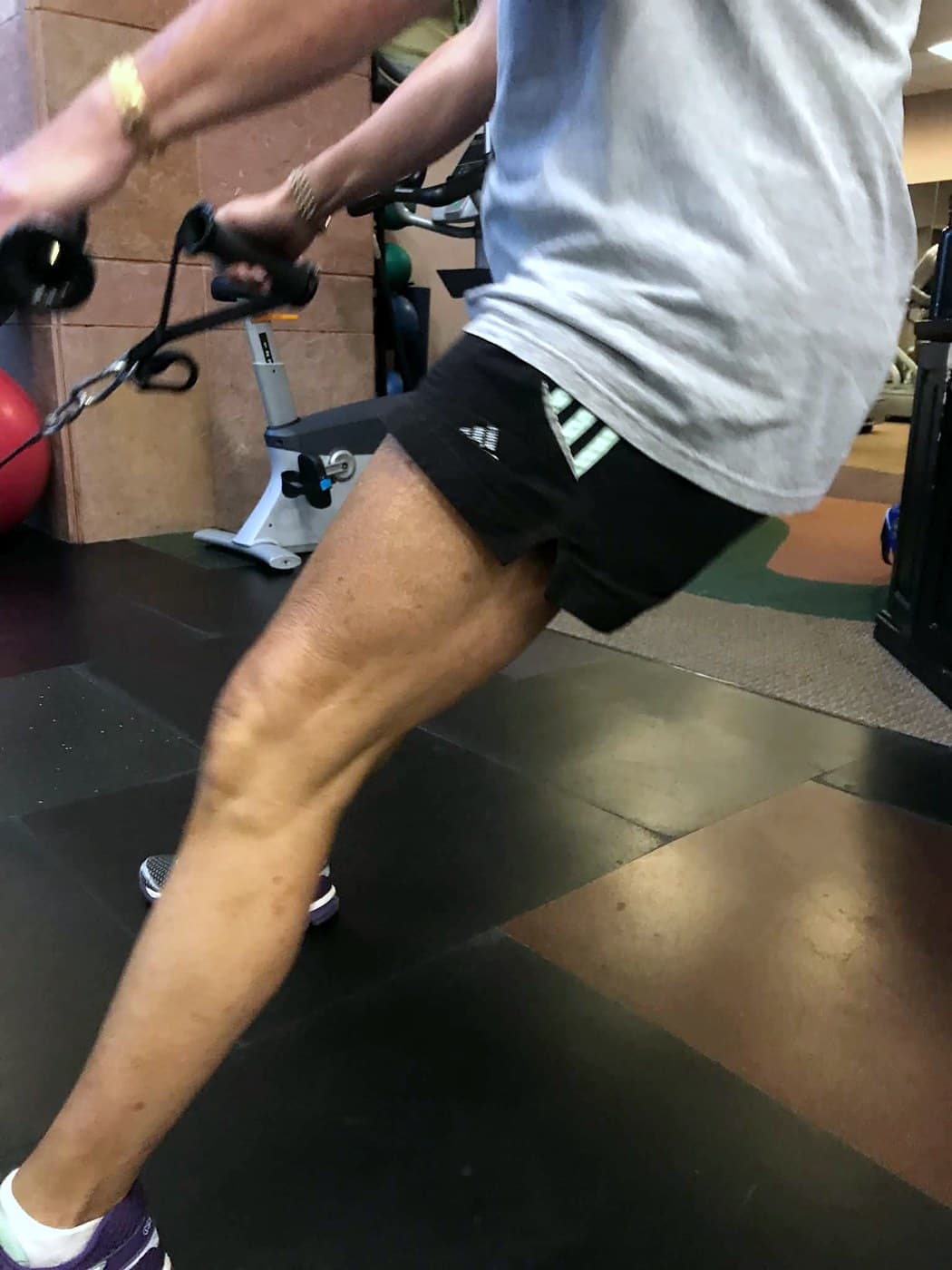 A client in a split stance drawing a cable handle toward her, mid-repetition.