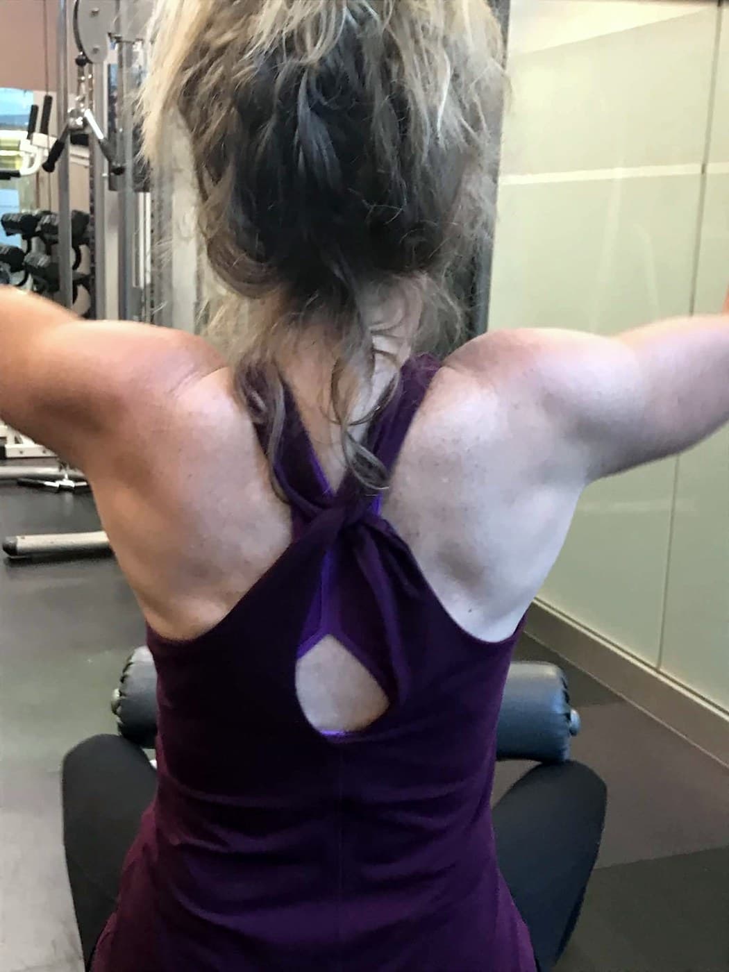 A client seen from behind, arms wide overhead, pulling down on a lat bar.