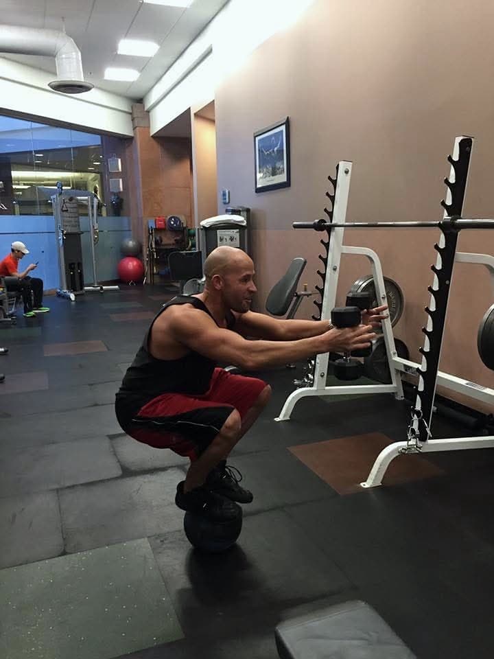 Keith Banner holding a squat while balanced on a medicine ball, arms extended to a rack.