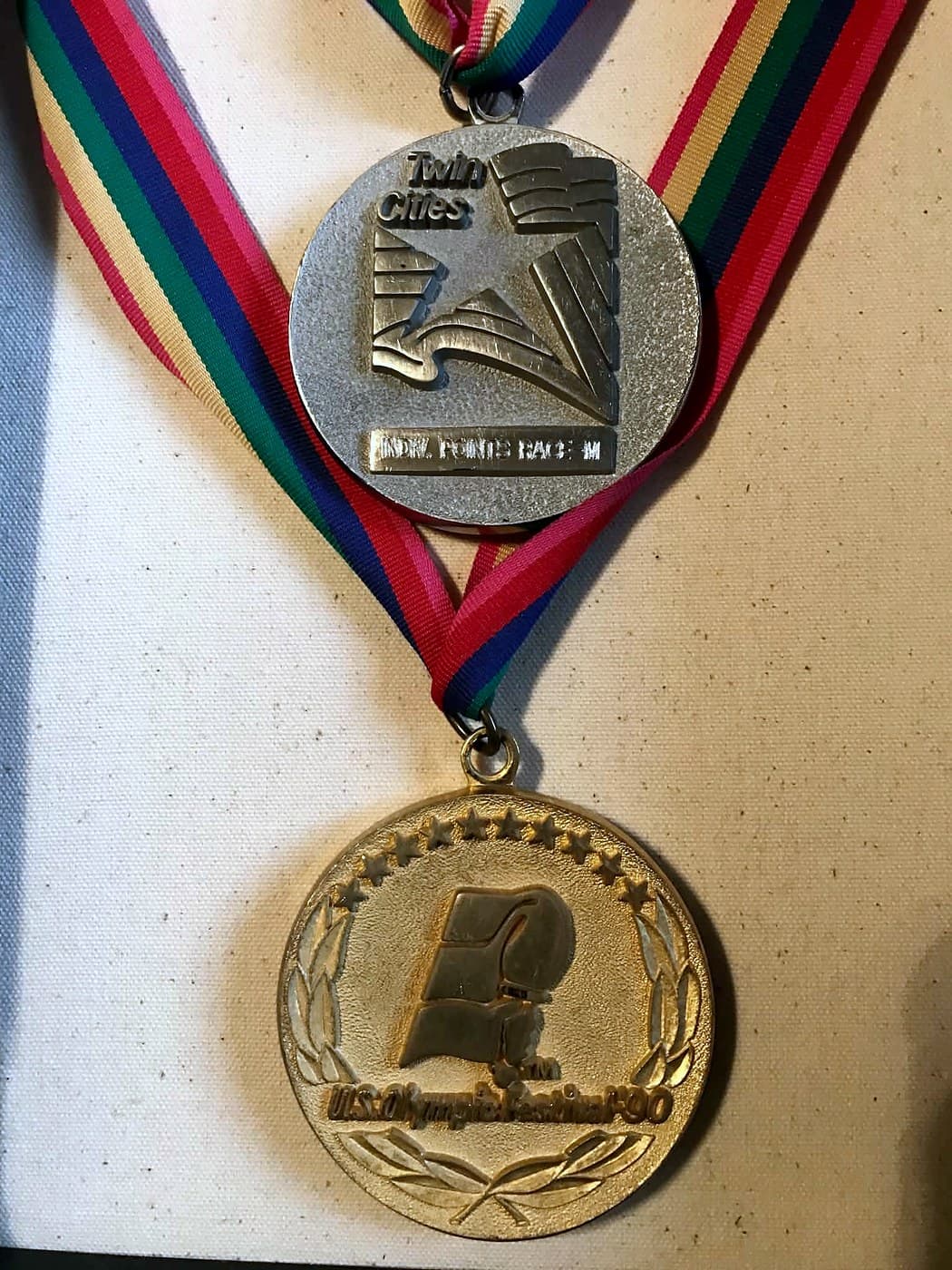 Two medals on striped ribbons: a gold U.S. Olympic Festival '90 medal and a silver Twin Cities medal engraved 'Indiv. Points Race'.