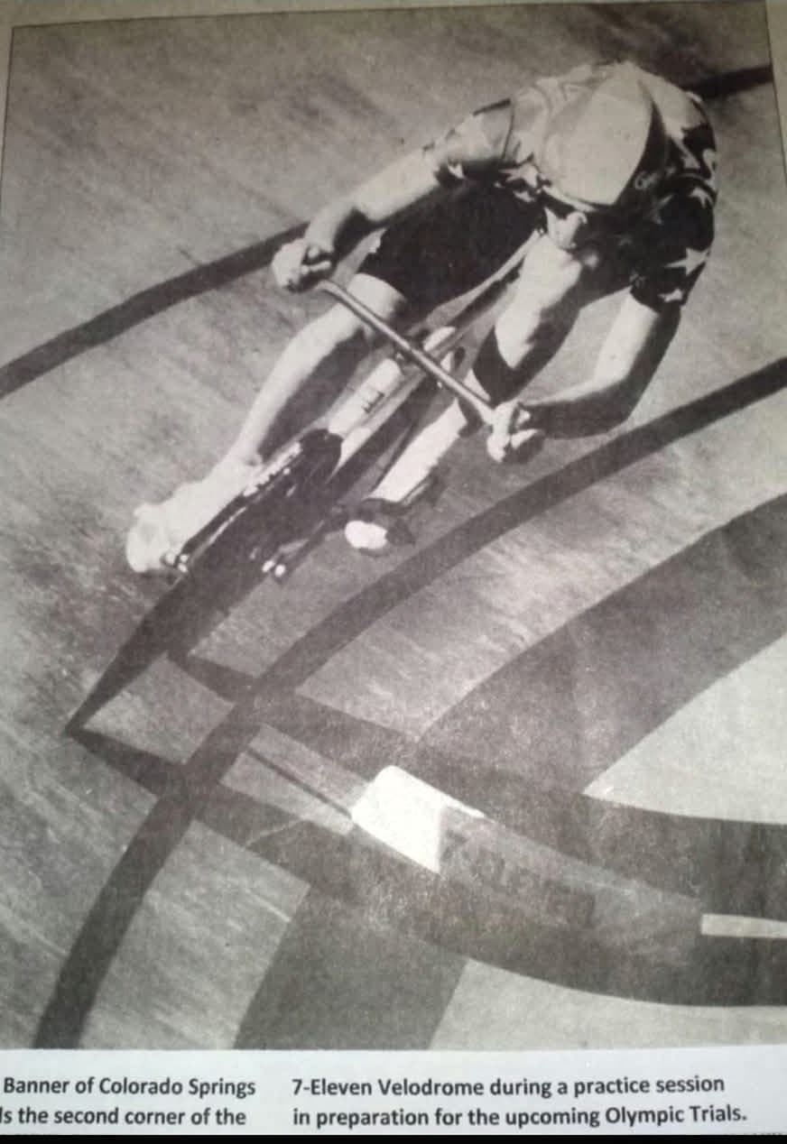 Black and white newspaper photograph of Keith Banner riding high on the banking of a velodrome track.